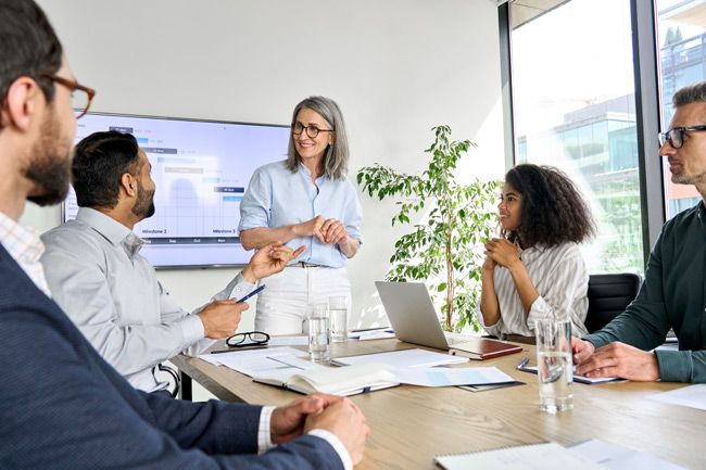 exec woman standing team at table shutterstock 2021639267 650x433