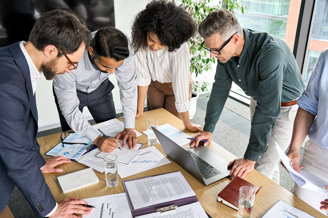 team standing looking at table shutterstock 2165394867 650x433